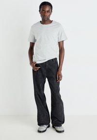 Grå bomulds T-shirt med korte ærmer, parret med løstsiddende sorte denim jeans. Modellen bærer grå strukturerede sko og står i en neutral baggrund.