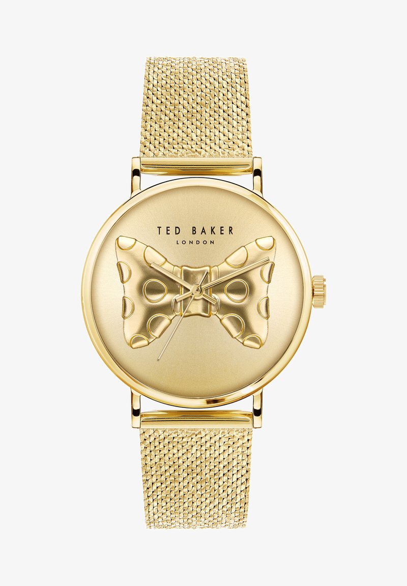 Zlaté analógové hodinky s textúrovaným sieťovým remienkom, s dizajnom motýlika na ciferníku, doplnené bodkovanými vzormi a názvom značky.