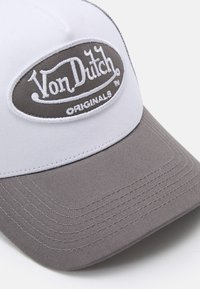 Siva i bijela kapa s zakrivljenim vizirima, sa istaknutim ovalnim zakrpa na kojoj piše "Von Dutch ORIGINALS" u bijelom vezu. Teksturirana tkanina.