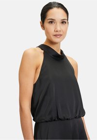Czarny top na halter z drapowanym wzorem i teksturowym materiałem. Posiada szeroki dekolt i marszczenia w pasie.
