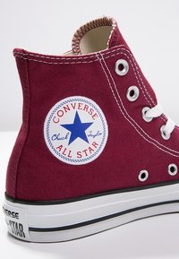 Baskets montantes bordeaux en toile, avec une semelle en caoutchouc blanc, des œillets en métal et un patch logo rond avec une étoile bleue.