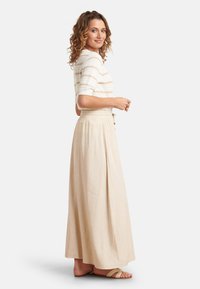 Witte gebreide top met horizontale beige strepen, gecombineerd met een lange, beige, vloeiende rok met een geraffineerde taille en knoopdetails.