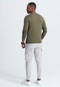 Camicia verde oliva a maniche lunghe, vestibilità slim, con pantaloni cargo beige, dotati di tasche. Indossata con sneakers bianche. Design semplice e colori neutri.