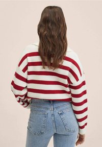 Pull côtelé rayé rouge et blanc avec manches larges, associé à un jean taille haute bleu clair. Détail arrière et texture visibles.