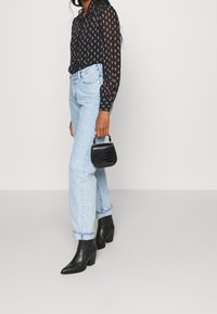 Sort langærmet bluse med små blomsterprint, lyseblå lige ben jeans, sorte hælede ankelstøvler og en lille sort håndtaske.
