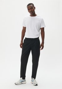 Pantaloni neri con un design sartoriale, tessuto leggero e texture liscia. Abbinati a una t-shirt bianca semplice e sneakers argento.