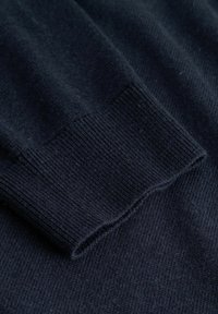 Prążkowany ciemnogranatowy materiał swetra o miękkiej fakturze z ściągaczami przy rękawach. Materiał wygląda na dzianinę, podkreślając gładkość i równomierne wykończenie.