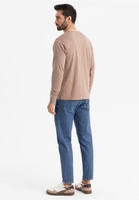 Hellbraunes Langarmhemd, blaue Jeans und weiße Sneakers mit braunen Akzenten, von hinten vor einem weißen Hintergrund betrachtet.