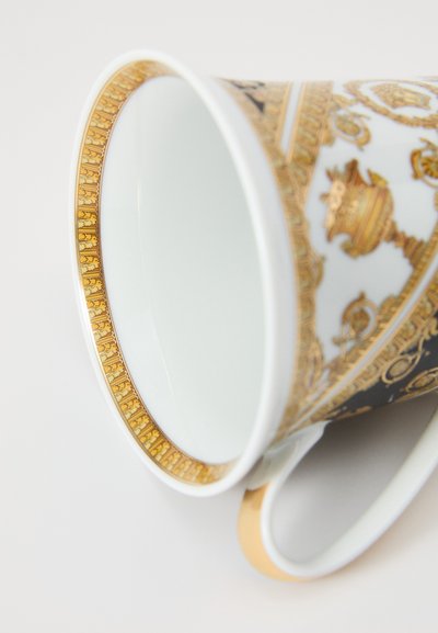 Διακοσμητικό πορσελάνινο φλυτζάνι με χρυσές λεπτομέρειες, περίπλοκα σχέδια και λείο λευκό εσωτερικό. Η λαβή διαθέτει διακριτική χρυσή επένδυση.