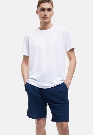 T-shirt bianca a maniche corte con scollatura rotonda abbinata a pantaloni corti navy in tessuto, dotati di tasche e dal fit rilassato.