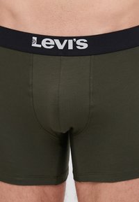 Maslinaste pamučne bokserice sa crnim elastičnim pojasom na kojem se nalazi bijeli "Levi's" logo. Glatka tekstura, prilagođen dizajn.