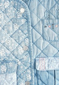 Gepolsterte Jeansjacke in Hellblau mit floralem Stoff. Verfügt über silberne Knöpfe, kontrastierende Nähte und zwei vordere Taschen mit dekorativen Akzenten.