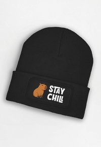 Black knit beanie with a folded cuff, featuring a beige capybara illustration and the text "STAY CHILL" in white on a black patch.