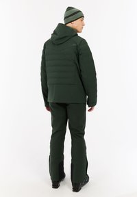 Tamsiai žalia izoliuota striukė su kapišonu, derinama su atitinkančiomis žaliosiomis kelnėmis. Šis komplektas pasižymi optimizuotu dizainu ir matomais užtrauktukais.