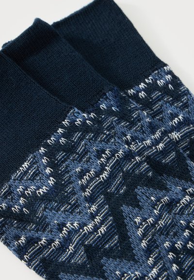 Paire de chaussettes en tricot bleu marine avec des motifs géométriques dans des nuances de bleu et blanc sur fond blanc.
