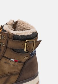 Stivale alla caviglia in pelle marrone con rivestimento in pelliccia sintetica, polsino in tessuto, fibbia metallica e dettagli accentuati tra cui un logo e una striscia colorata vicino alla suola.