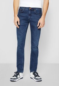 Temno modri jeans z ožjim krojem, petimi žepi in vidno šivanim detajlom, dopolnjenim z gumbom in zadrgo.