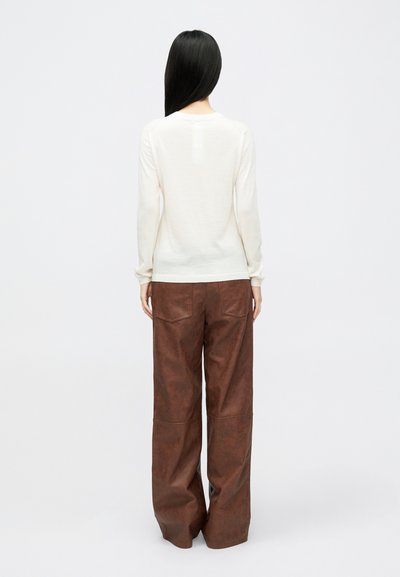 Top de manga longa em creme combinado com calças largas de imitação de couro castanho, apresentando bolsos traseiros e um acabamento suave e texturizado.