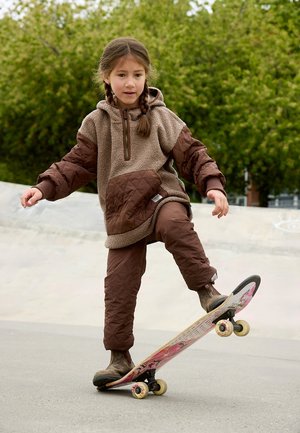 Braune Fleece-Hoodie mit steppbaren Ärmeln, kombiniert mit braunen gesteppten Hosen. Das Kind fährt auf einem Brett mit grafischem Design.