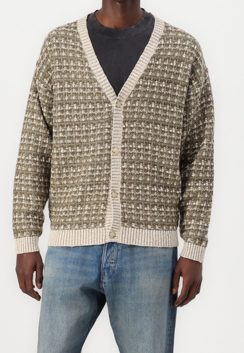 Stickad kofta i olivgrönt med vitt mönster. Har V-ringning och beige ribbad kant, stängs med knappar fram.