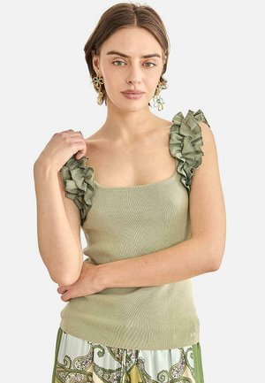 Mujer con blusa sin mangas verde claro con tirantes con volantes y pantalones con estampado floral, complementada con grandes pendientes florales.