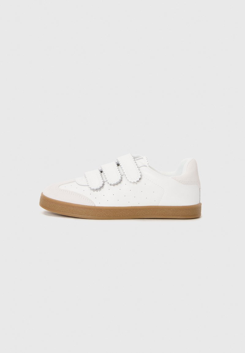 White sneaker with velcro straps, perforated design on the sides, light grey accents, and a tan rubber sole. Rounded toe shape.