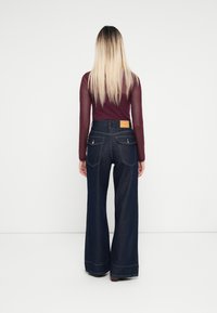 Bredde ben mørk denim jeans med høy midje, med et lærmerke bak og to baklommer. Kombinert med en tettsittende mørkerød topp.