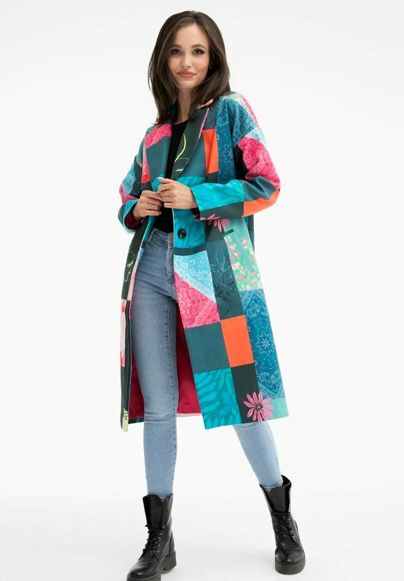 Barevný patchworkový kabát s různými vzory v barvách tyrkysové, růžové a oranžové, s knoflíkovým zapínáním a hladkým povrchem. Nositelný přes džíny a boty.