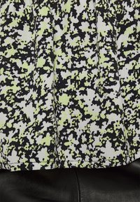 Tecido preto e branco com um padrão abstrato aleatório de manchas verde-lima e cinza, apresentando uma textura suave e bordas acabadas.