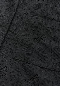 Tissu noir texturé avec un motif ondulé, présentant des éléments semblables à du maillage et des zones lisses, créant un contraste visuel et de la profondeur.