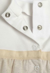 Weißer, weicher Stoff mit einem Kragen, silbernen Druckknöpfen und einem beigen Bündchen. Besitzt einen durchsichtigen Tüllrock mit goldenen Sprenkeln.