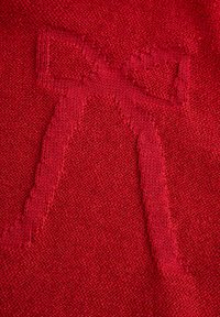 Czerwona dzianina z haftowanym wzorem kokardy. Tekstura jest gładka, z jednolitym wzorem ściegów na całej powierzchni.