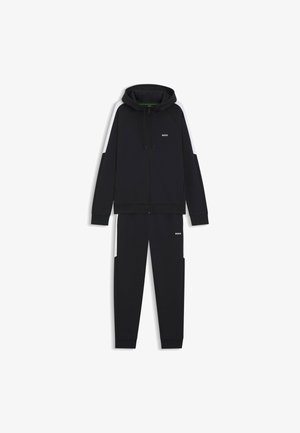 Setti, joka koostuu mustasta hupparista ja housuista, joissa on vetoketjukiinnitys, huppu ja logotunnukset. Valmistettu pehmeästä kankaasta, jossa on kontrastiväriset valkoiset sivupaneelit.