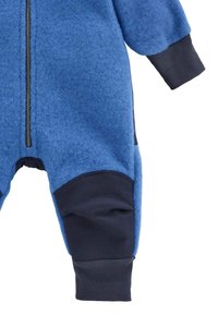 Blauwe fleecedons met een rits over de volledige lengte. Het heeft donkerblauwe accenten op de manchet en knieën, wat voor textuurcontrast zorgt.