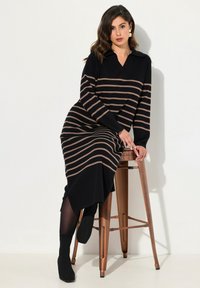 Robe tricotée à manches longues, avec des rayures horizontales noires et beiges, un col en V et une fente latérale, associée à des bottines noires.