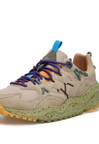 Sneaker beige in suede e mesh con lacci viola e blu, accenti gialli, suola verde maculata e una linguetta posteriore texturizzata. Design slanciato.