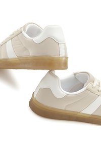 Beige synthetic sneakers with white accents, smooth texture, round toe, and rubber soles. Includes laces and a padded collar detail.