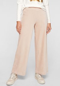 Pantalon en velours côtelé rose clair à jambes larges, avec une texture côtelée verticale et une ceinture élastique. Assorti à des baskets à plateforme beige.