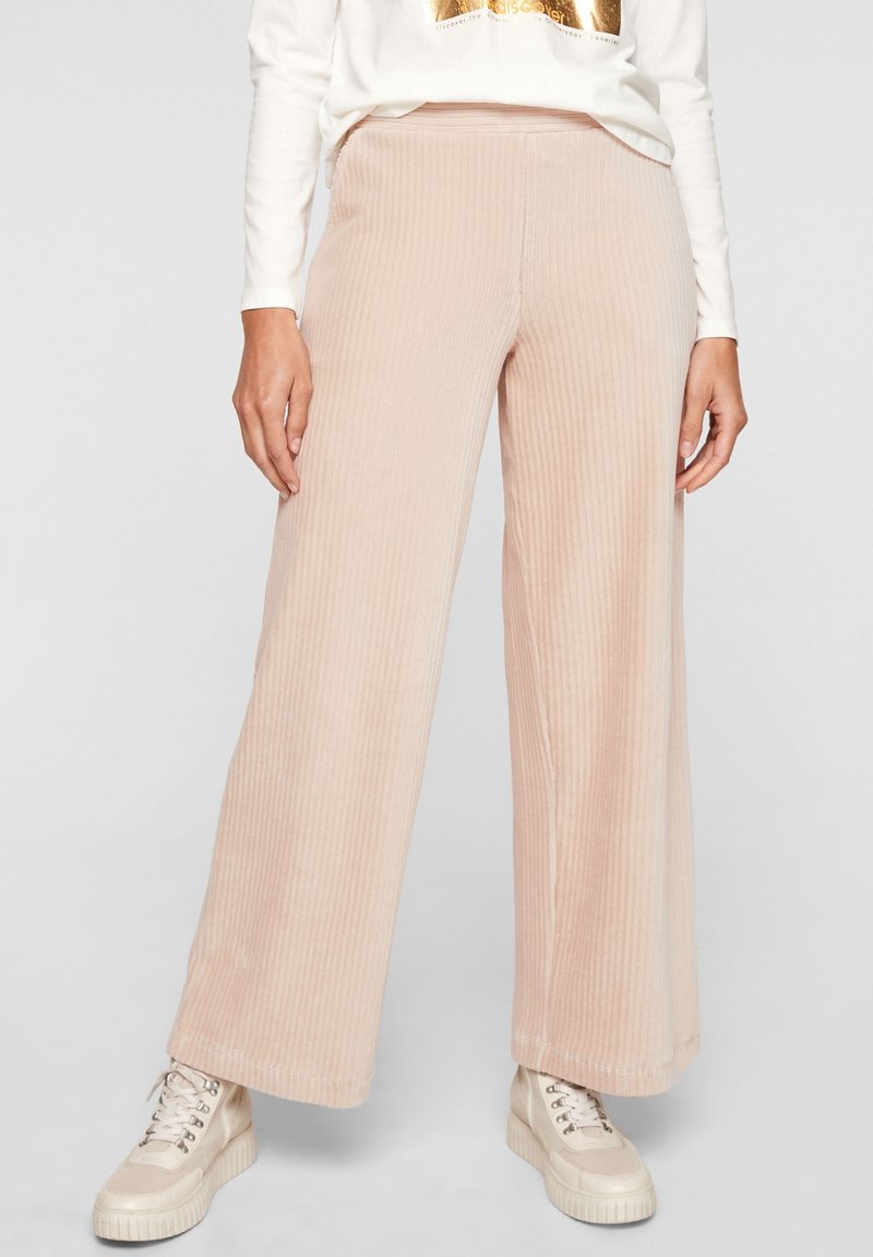 Pantalon en velours côtelé rose clair à jambes larges, avec une texture côtelée verticale et une ceinture élastique. Assorti à des baskets à plateforme beige.