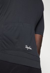 Crna biciklistička majica izrađena od lagane tkanine. Ima stražnji džep i bijeli logo "Rapha". Kratki rukavi sa aerodinamičnim dizajnom.