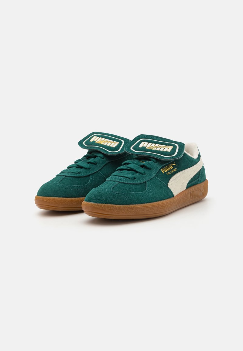 Sneakers in suede verde con una striscia in pelle bianca, caratterizzati da doppie cinghie in velcro e suole in gomma. Logo con dettagli dorati sulle cinghie.