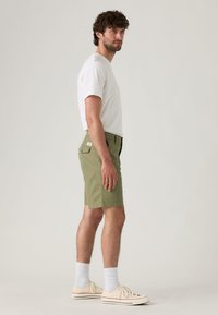 Shorts vert olive en mélange de coton, dotés d'un devant plat, de poches latérales et d'une poche plaquée à l'arrière. Associés à un t-shirt blanc.