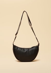 Sac à bandoulière noir texturé en forme de croissant avec sangle rayée réglable et pièces métalliques dorées sur fond beige.