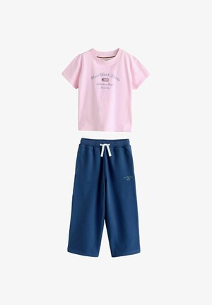 Rosa Kurzarm-T-Shirt mit dem Schriftzug "New York State" und einer Flagge darüber, kombiniert mit blauen, weit geschnittenen Hosen mit weißem Kordelzug an der Taille.