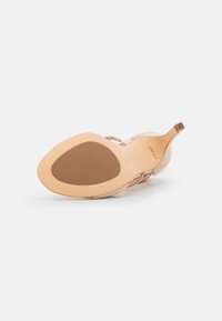 Sandal de tacón alto con una parte superior de suave ante beige, un diseño de tiras elegante, punta afilada y una suela de goma marrón. Detalle de marca minimalista.