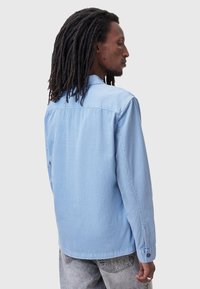 Lichtblauwe denimshirt met een klassieke kraag, lange mouwen en knopenmanchetten. Heeft een rechte rugontwerp en minimale stikdetails.