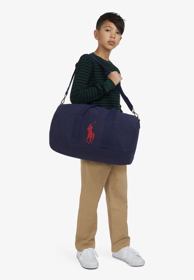 Bolsa de lona azul marino con logo bordado en rojo, que cuenta con dos asas, correa de hombro ajustable y acabado de tela texturizada.