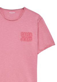 Camiseta de manga corta de color rosa claro con cuello redondo y un logo texturizado de "SALSA JEANS" en el lado izquierdo del pecho. Fabricada con un material suave y ligero.