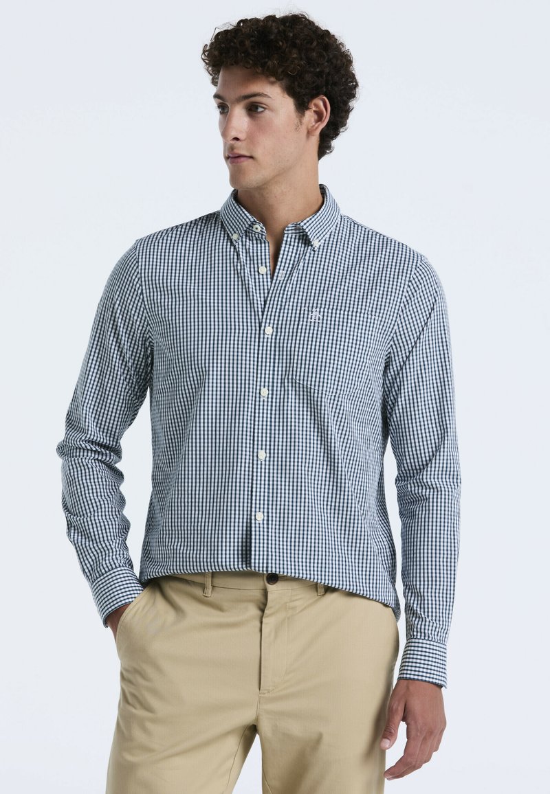 Gekleurde button-down shirt in marineblauw en wit, met lange mouwen en een kraag. Draagt een beige broek. Heeft een klein logo op de borst.