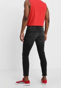 Vaqueros negros ajustados con una textura suave, bolsillos traseros y dobladillo sin rematar. Combinados con zapatillas de skate rojas con un patrón de tablero de ajedrez.